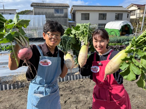 収穫した大根とカブを持つ、たむたむと難波リポーター